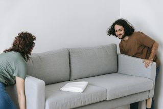 A couple working together to adjust a gray sofa inside a cozy living room space.