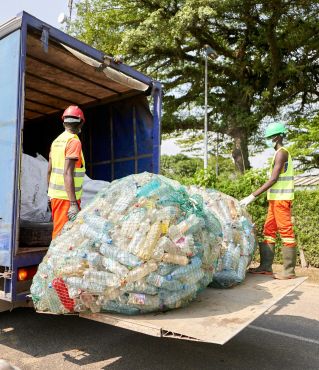 Two workers in protective gear loading plastic bottles onto a truck outdoors.